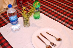 A table with a bottle of Aquafina water, a green Sprite bottle, a vase with flowers, and a plate with cutlery.