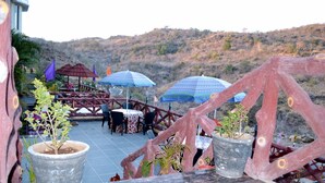 Un espace extérieur aménagé avec des tables et des chaises, entouré de plantes en pot et de parasols.