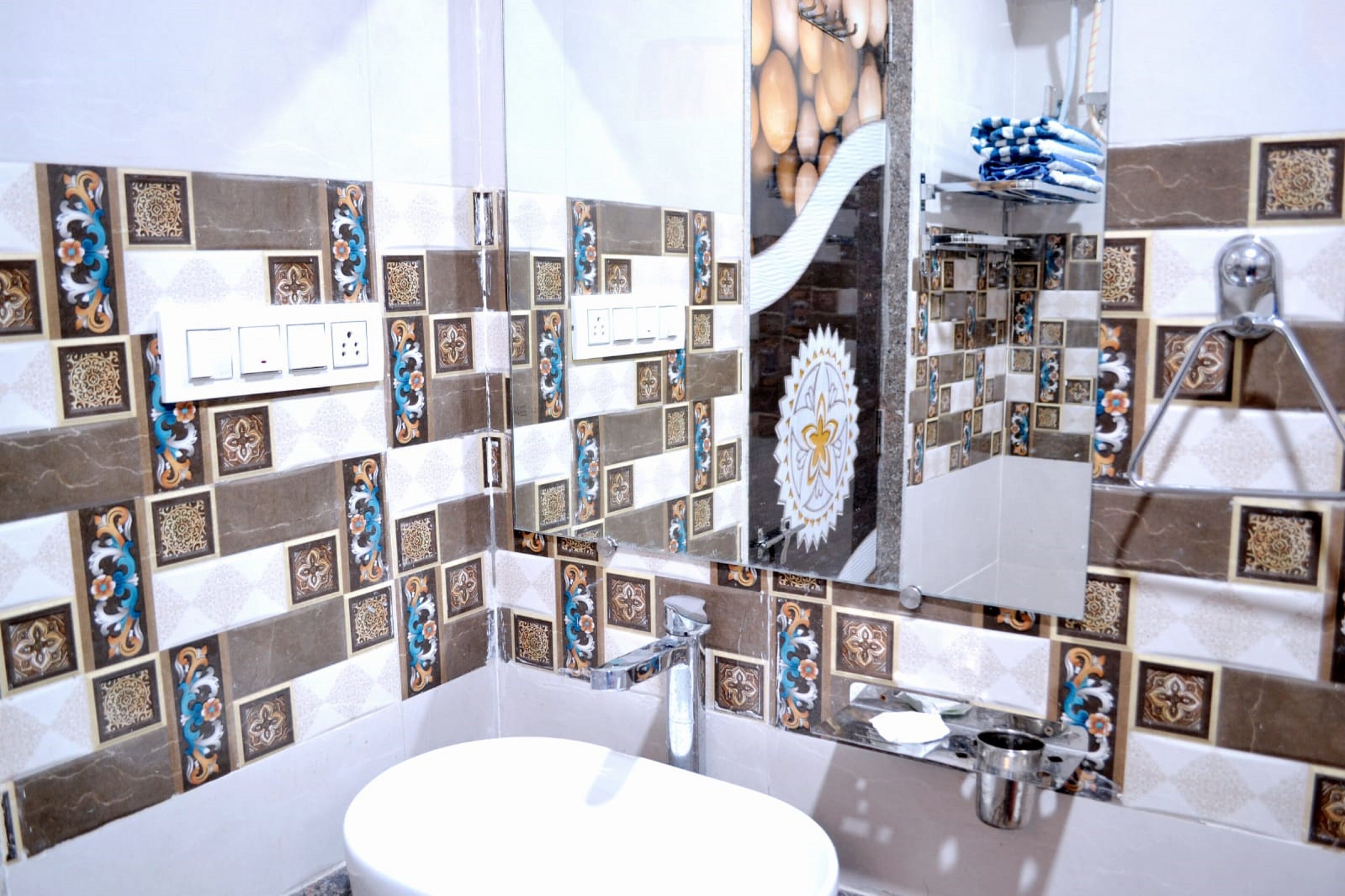 Baño con lavamanos blanco, espejo y zona de ducha. Las paredes están decoradas con azulejos estampados.