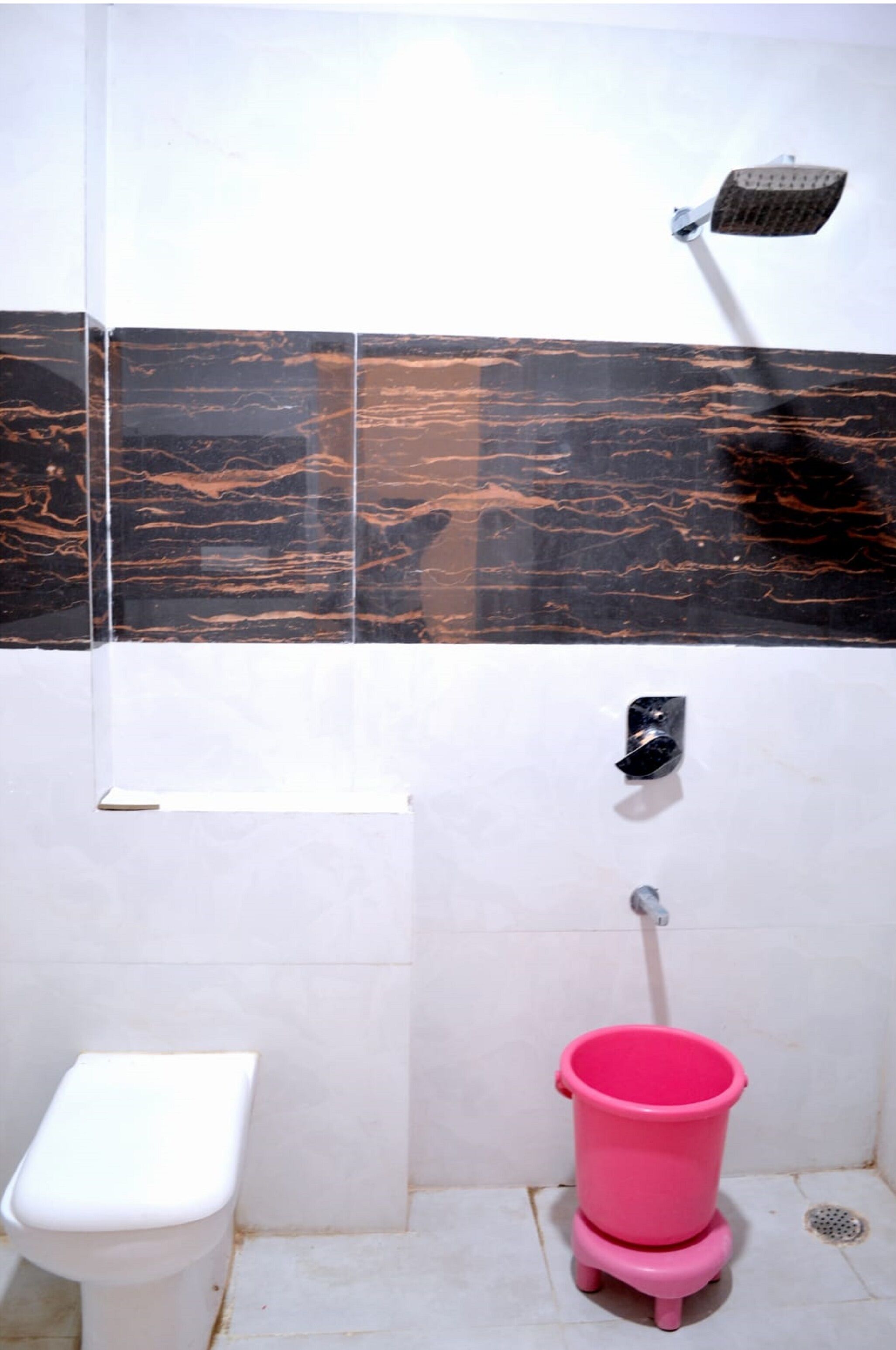 Une salle de bain avec des toilettes, un seau rose et une pomme de douche.