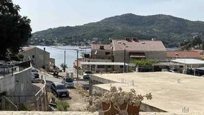 Un pueblo costero con vista al mar y colinas al fondo. Se observan edificios con techos de tejas rojas y un amplio espacio de concreto despejado en primer plano.
