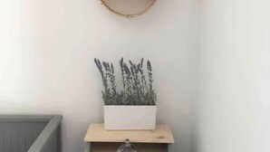 Un rincón con un armario gris, una maceta blanca con plantas y un estante redondo en la pared.