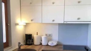 Cocina compacta con armarios blancos, lavavajillas integrado, cafetera y estufa.