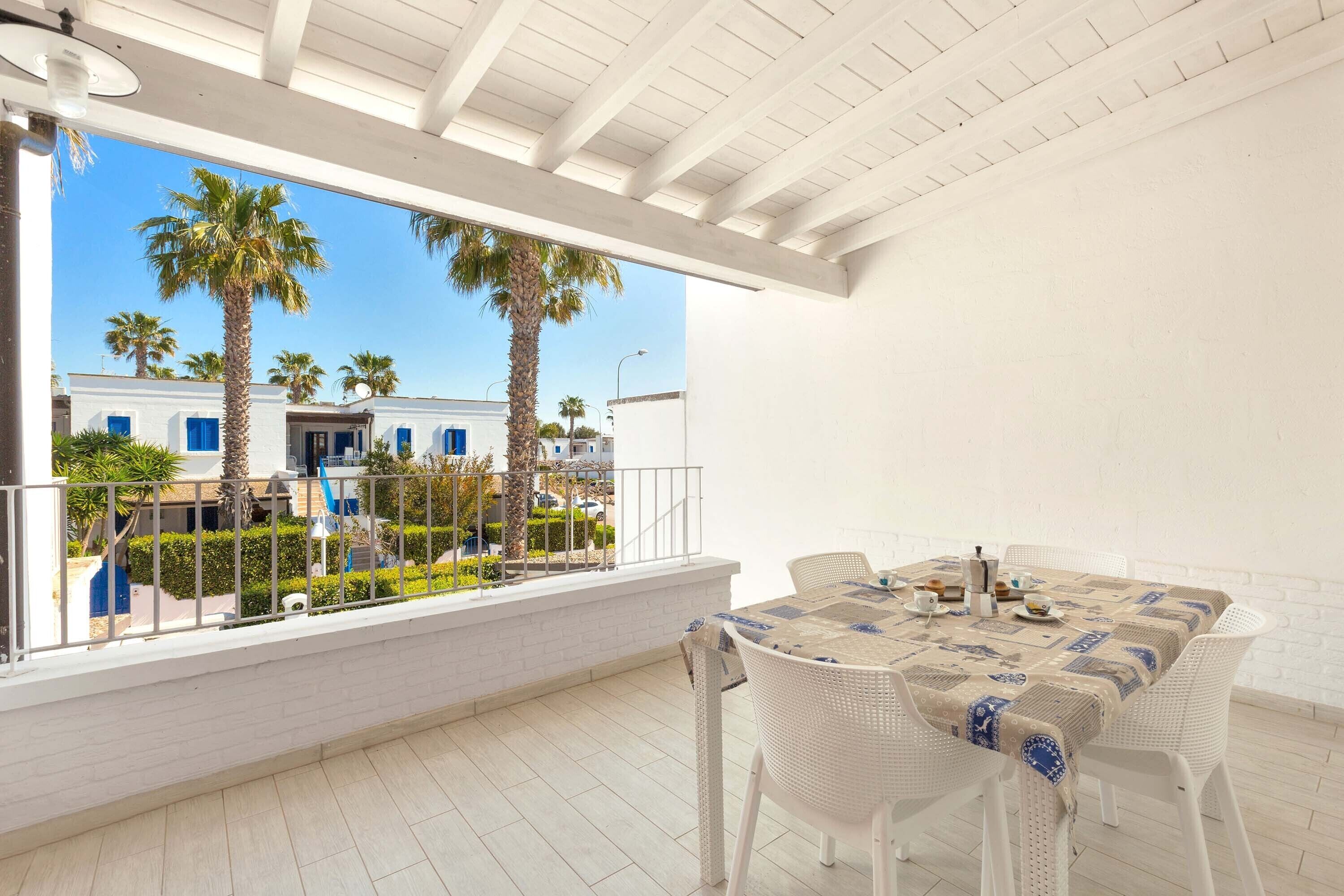 Un balcón con mesa y sillas, con vistas a un patio con palmeras y edificios.