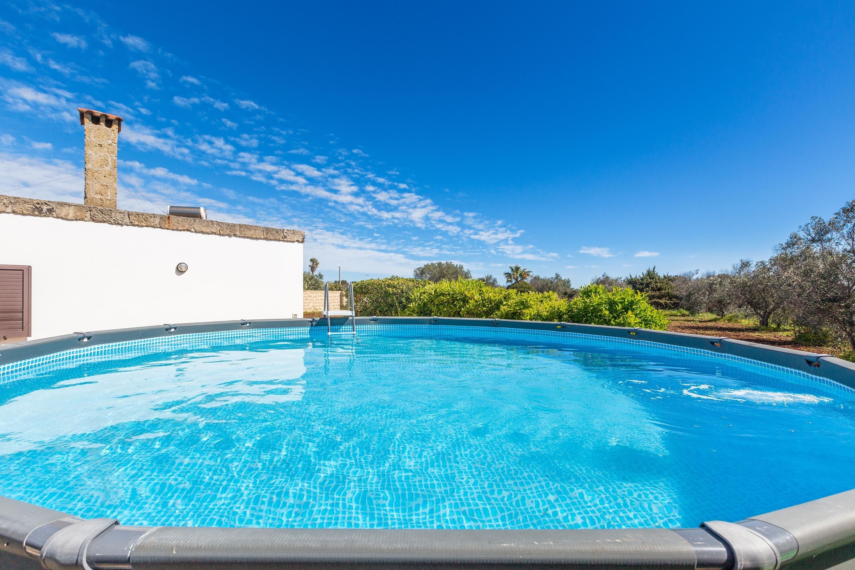 A swimming pool with a tiled edge, a stone chimney, and a white wall.