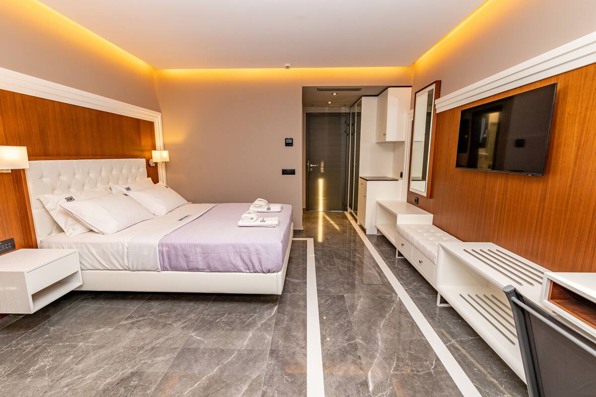 A modern hotel room with a large bed, bedside tables, a TV, and a walk-in closet.