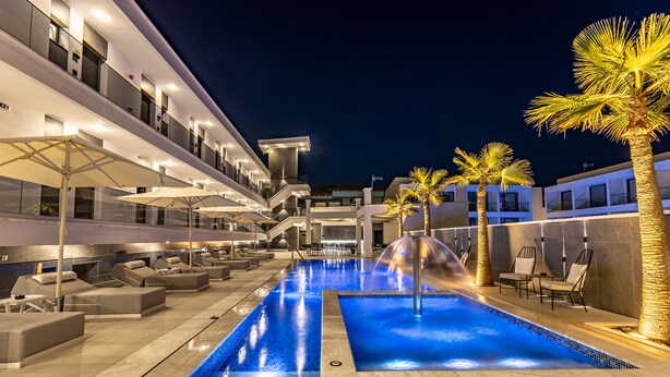 Un área de piscina moderna con varios niveles, sillas de descanso y palmeras.