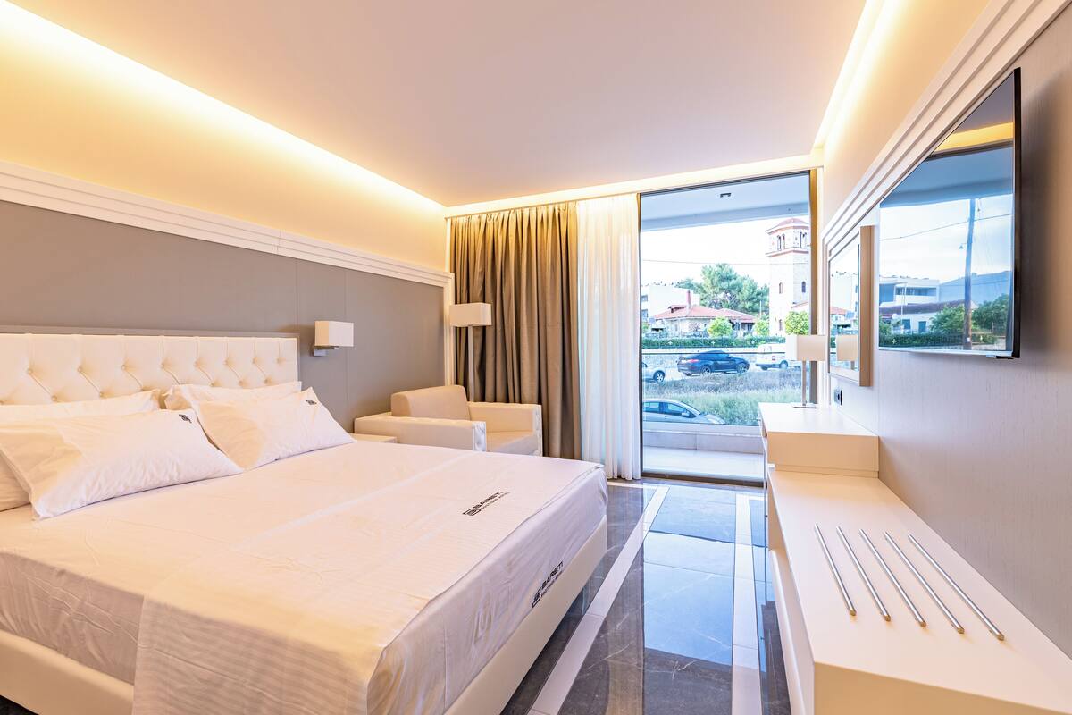 A modern hotel room with a large bed, a desk, and a view of the outside.