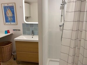 Une salle de bain avec un lavabo blanc, un miroir et un rideau de douche.