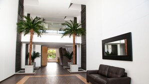 Een moderne lobby met een bruine leren bank, twee palmstruiken en een grote spiegel aan de muur.