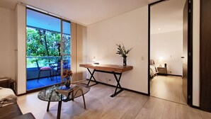 Een moderne kamer met een glazen tafel, een houten bureau en uitzicht op groen.