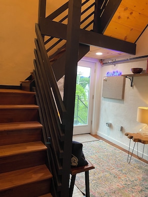 En trætrap med gelænder i mørk farve fører op til en dør med et glasfelt. En neonskilte står der: "Good Vibes".