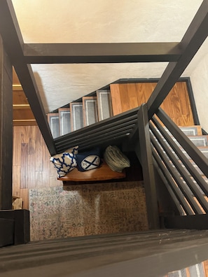 Una escalera con barandilla de madera y un estante con almohadones decorativos y una alfombra.