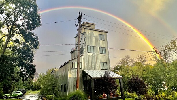 Un bâtiment à deux étages doté d’un porche, entouré de verdure et avec un arc-en-ciel bien visible dans le ciel.