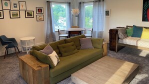 Un salon chaleureux avec un canapé vert, une table basse en bois et un coin repas comprenant une table ronde et des chaises.