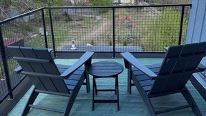Un balcon avec deux fauteuils et une petite table, donnant sur un quartier résidentiel avec des maisons et un ciel dégagé.