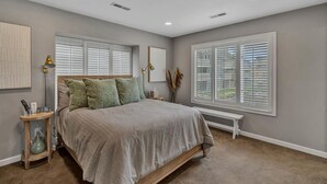 Ein Schlafzimmer mit einem Bett, Nachttischen, einer Bank und einem Fenster mit Jalousien.