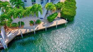 A waterfront property with a dock, palm trees, and a house with a balcony overlooking the water. - Winter Sale! Cabana Club, Dock, Kayak Launch, Pet Friendly (Key Colony Beach)