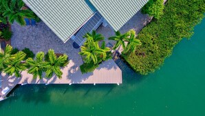 An aerial view of a waterfront property with a wooden deck, palm trees, and a building with a green roof. - Winter Sale! Cabana Club, Dock, Kayak Launch, Pet Friendly (Key Colony Beach)