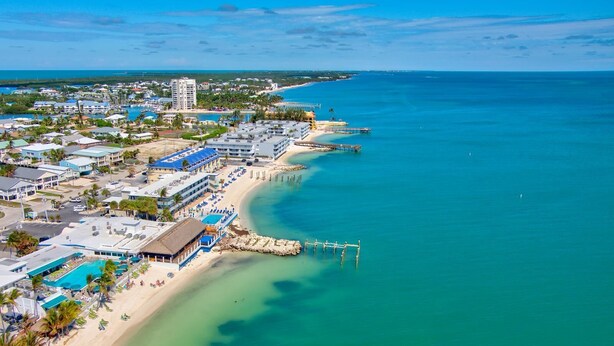 An aerial view of a coastal resort with a beach, a pier, and a hotel with multiple buildings and a pool area. - Winter Sale! Cabana Club, Dock, Kayak Launch, Pet Friendly (Key Colony Beach)