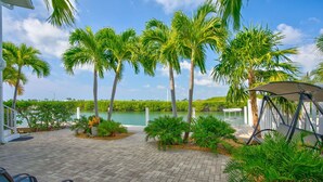 A paved patio with palm trees, a water body, and a covered seating area. - Winter Sale! Cabana Club, Dock, Kayak Launch, Pet Friendly (Key Colony Beach)