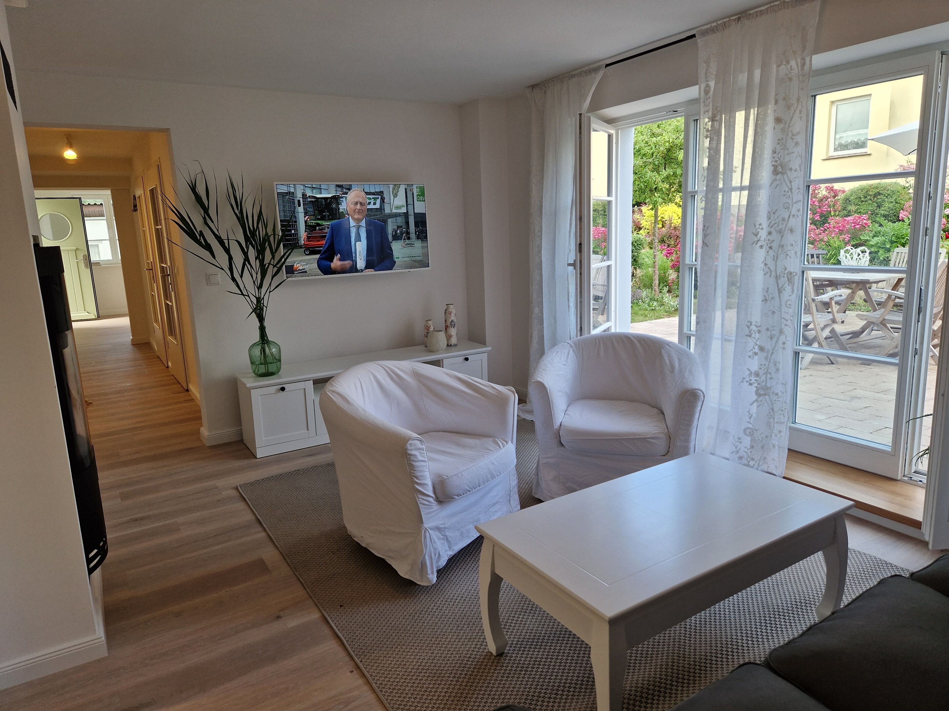 Ein modernes Wohnzimmer mit einer Couch, Sesseln, einem Couchtisch und einem an der Wand befestigten Fernseher.