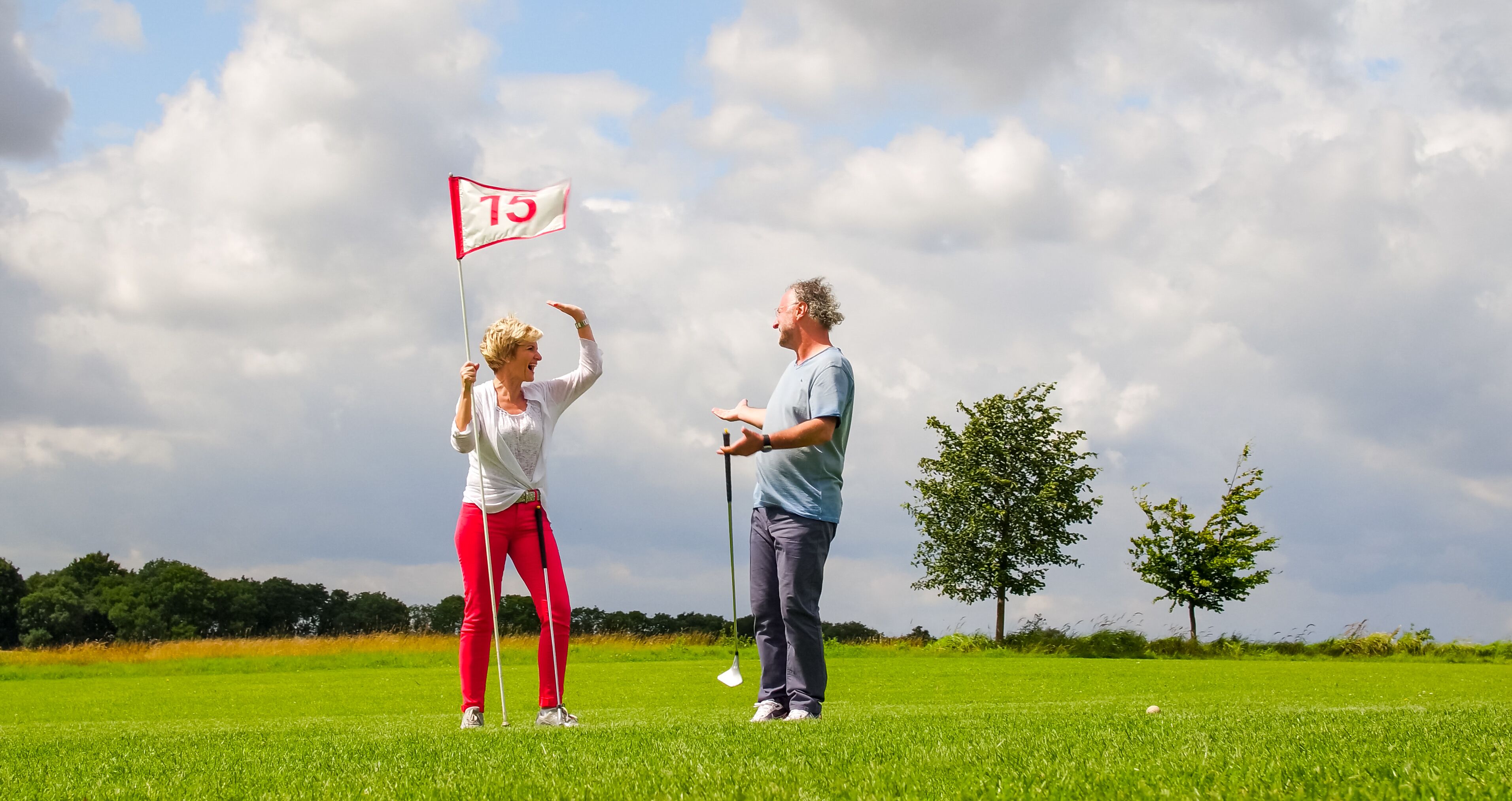 En golfbane med et flag markeret '15' og to personer på greenen.