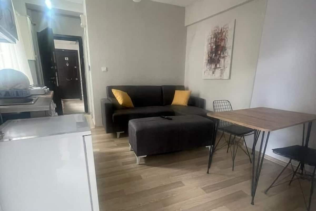 A modern living space with a sofa, ottoman, dining table, and chairs. A ceiling fan and artwork are visible.