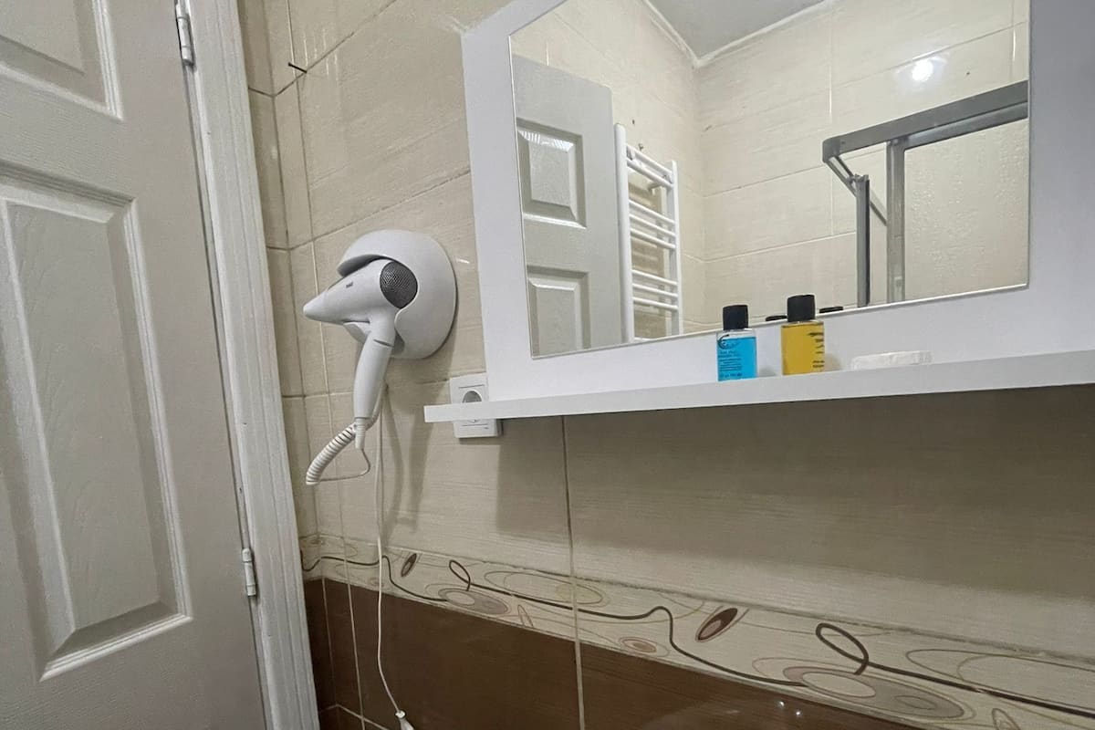 A bathroom with a white sink, a mirror, and a hairdryer mounted on the wall.