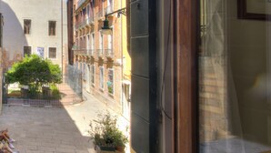 Une rue étroite bordée de bâtiments des deux côtés, un petit jardin entouré d’une clôture et un ciel bleu dégagé.
