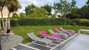 Área de piscina com espreguiçadeiras e deck coberto.