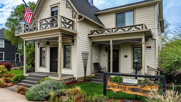 A two-story house with a porch, a flag, and a sign indicating it is for sale. - Historical John Rast House (Roseburg)
