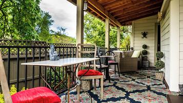 Eine Terrasse im Freien mit Holztisch und -stühlen, einem gemusterten Teppich und Topfpflanzen.