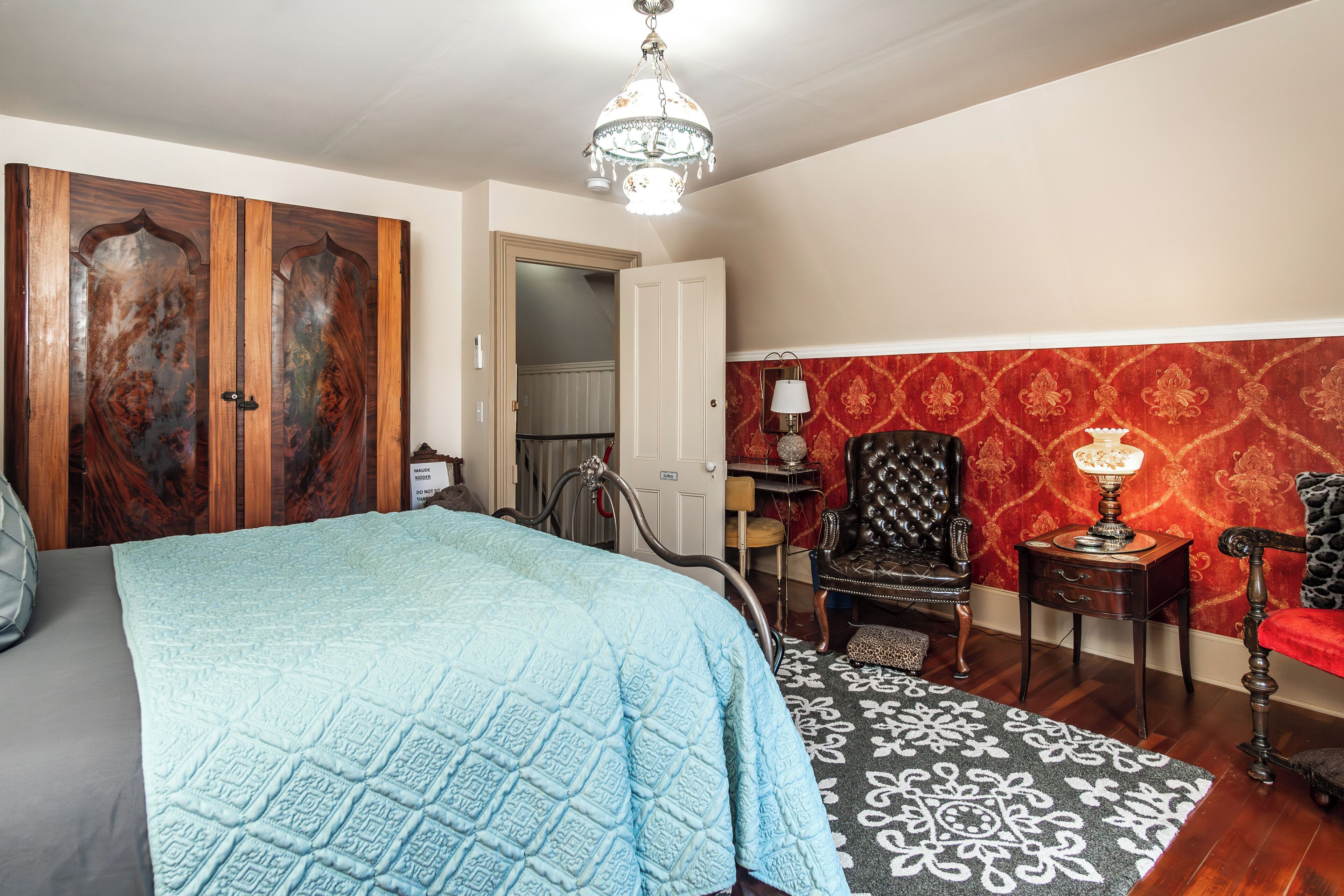 Un dormitorio con una cama grande, una araña de cristal, un pared con diseño rojo y un armario de madera.