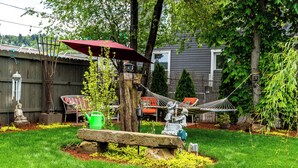 A backyard with a hammock, a statue, a stone bench, and a red umbrella. - Historical John Rast House (Roseburg)