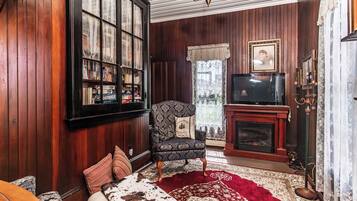 A cozy living room with a wooden paneled wall, a bookshelf, a patterned armchair, a red rug, and a fireplace.