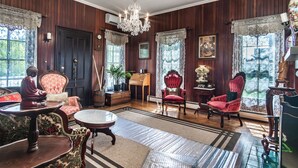 A traditional room with wooden paneling, a chandelier, and classic furniture including a red armchair and a wooden sideboard. - Historical John Rast House (Roseburg)