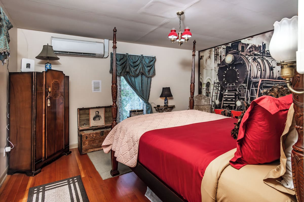 A bedroom with a large bed, wooden wardrobe, and a vintage-style lamp.