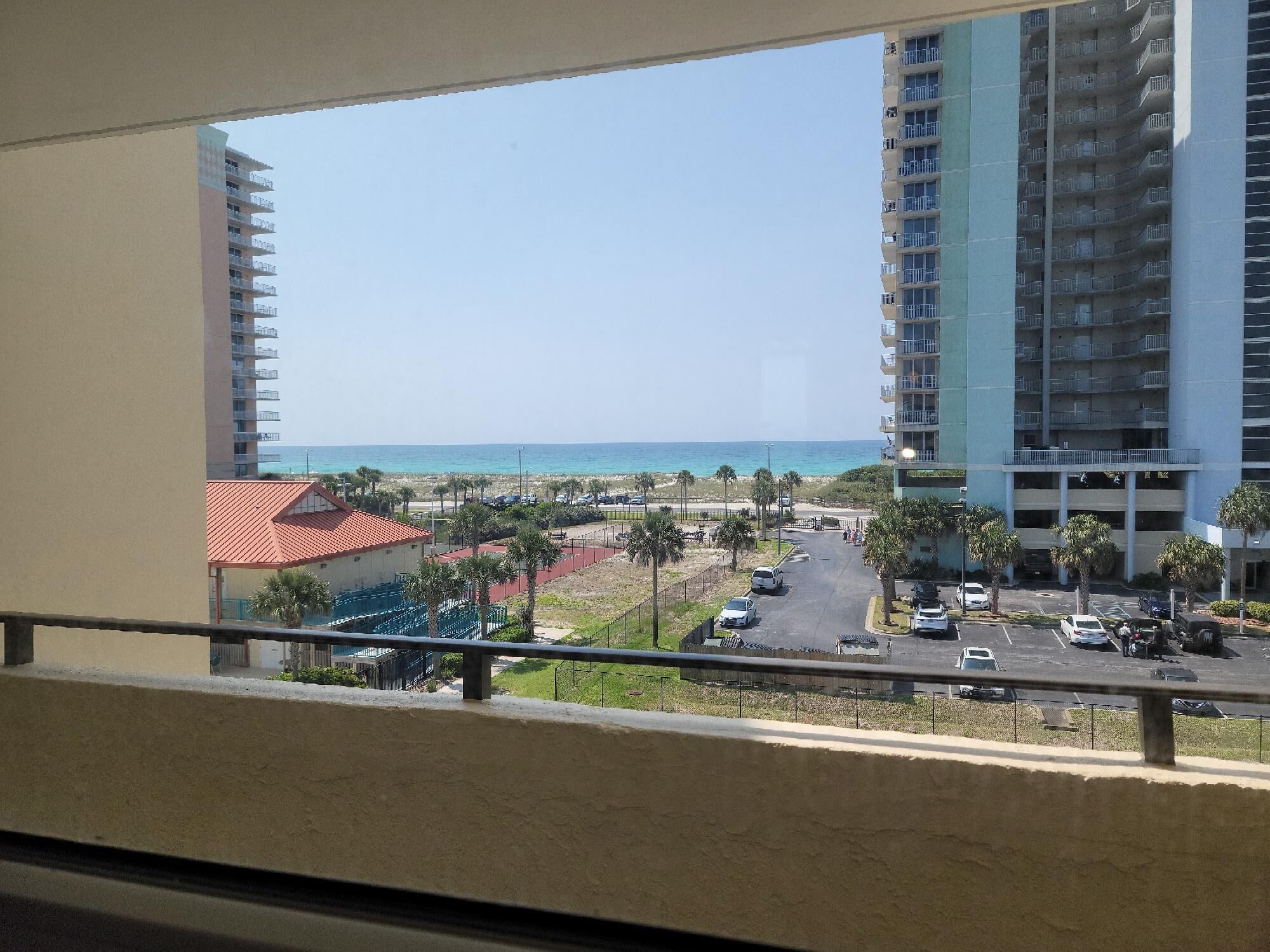 Blick vom Balkon auf einen Parkplatz mit Strand und Hochhäusern im Hintergrund.