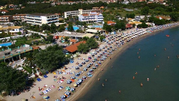 Un hotel sulla costa con diversi edifici, una spiaggia piena di ombrelloni e una zona dedicata al nuoto.