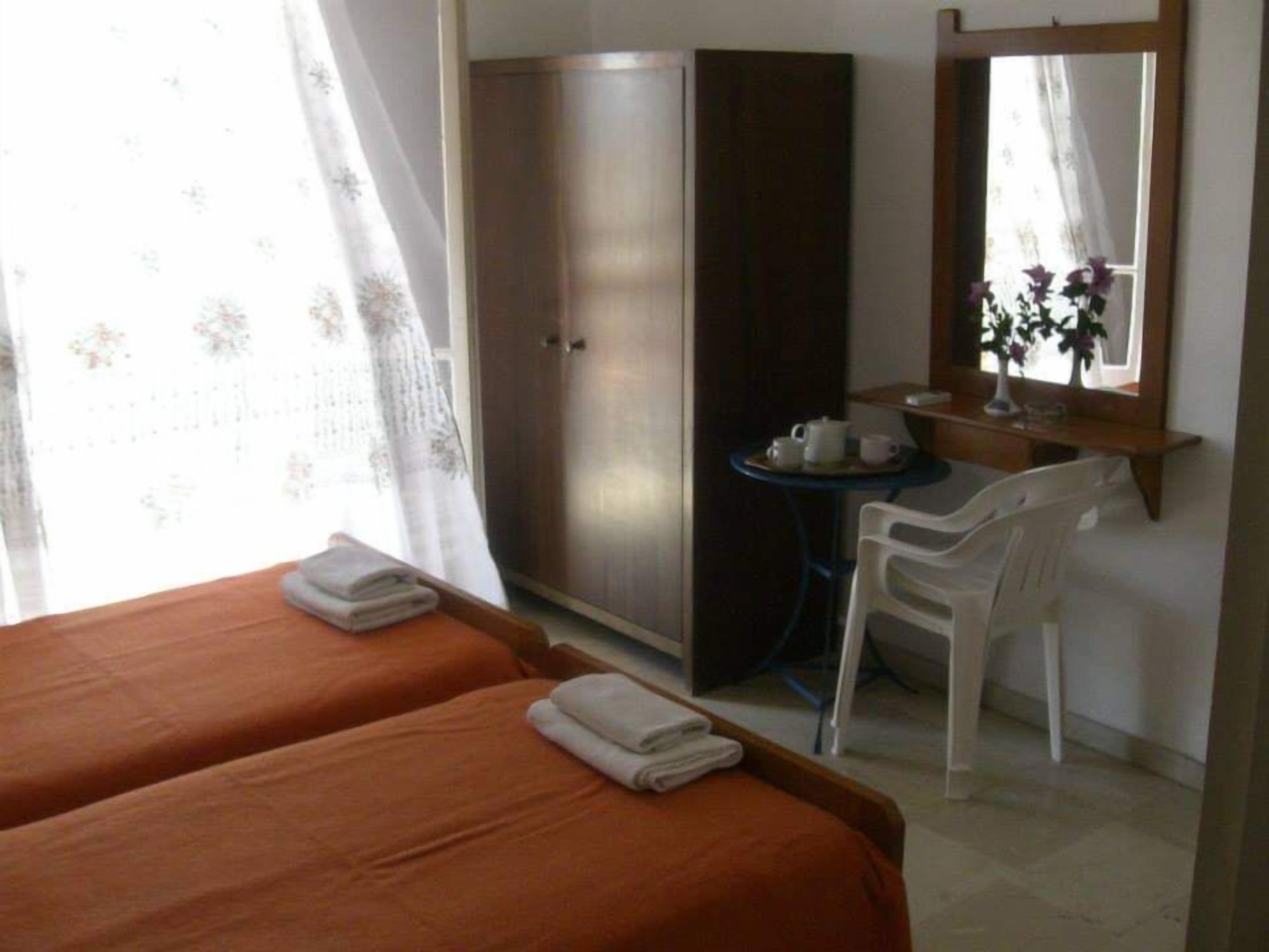 Habitació d'hotel amb dos llits, un armari, una taula petita amb una cadira i un mirall a la paret.