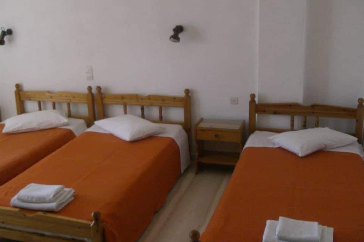 Een kamer met twee eenpersoonsbedden, elk met een oranje sprei en witte kussens. Daartussen staat een houten nachtkastje met een klein lade.