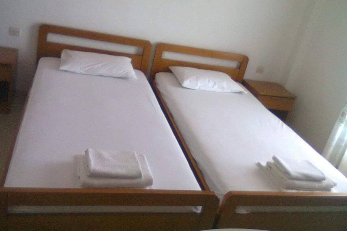 Twee eenpersoonsbedden met houten hoofdborden, witte lakens en opgevouwen handdoeken.