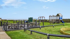 Un parque infantil con diversas estructuras de juego, mesas de picnic y una cerca de madera.