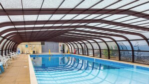 Una piscina interior con techo curvo y paredes de vidrio transparente que permiten vistas al exterior.