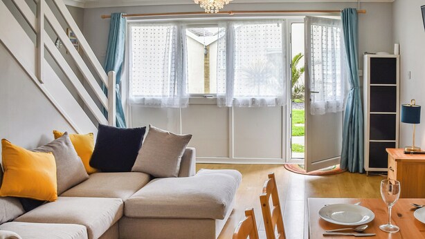 Una sala de estar con un sofá, una mesa de comedor puesta con platos, una copa de vino y una escalera.