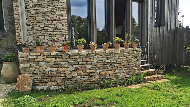 Eine Fassade aus Stein und Holz mit zahlreichen Fenstern und einer Holzterrasse.
