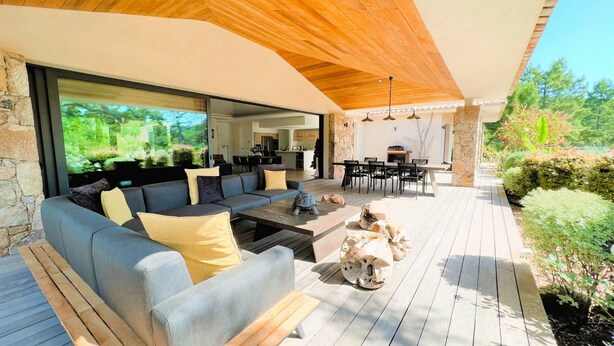 An outdoor living area with a sofa, coffee table, and a dining table with chairs. There is a stone pillar and a view of the garden. - Villa Pignotulli Di Cirendinu (sainte lucie de porto-vecchio)
