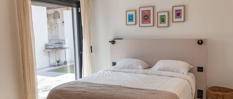 A bedroom with a bed, a bench, a wicker basket, and a view of an outdoor area.