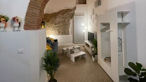 A modern interior with a brick archway, white walls, and a cozy seating area with a TV and shelving.